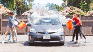 kids throwing buckets of water on a car for a car wash